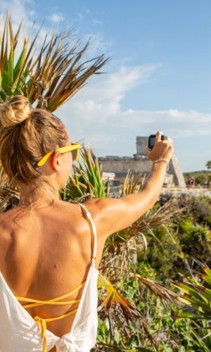 Young woman taking photo of ancient Mayan temple in Mexico having fun exploring while on vacations, Tulum