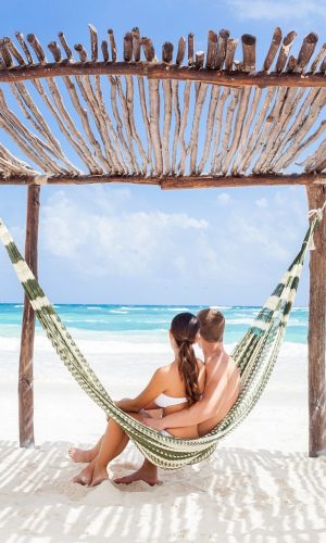 A happy young couple sitting on a hammock watching the ocean.